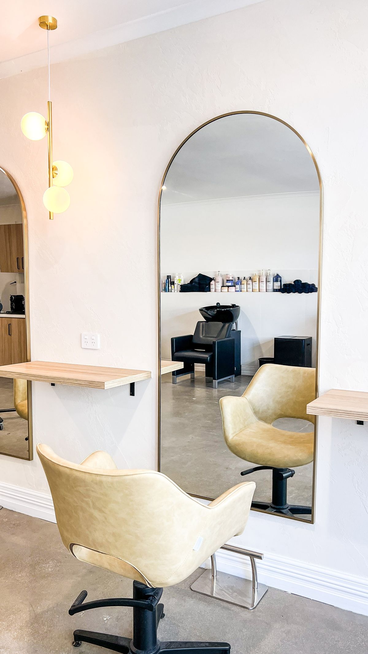 An arched mirror reflecting the wash area, beside a tan leather styling chair