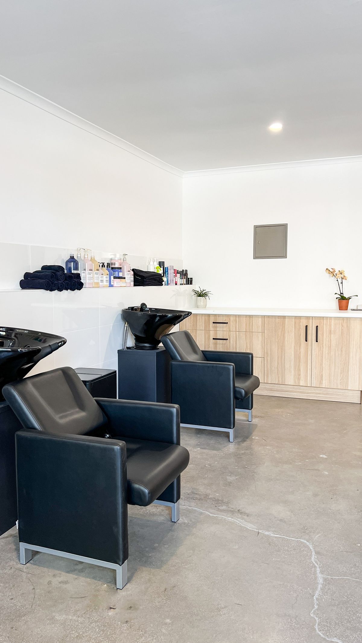 Two black leather backwash basins with timber cabinetry and polished concrete floors