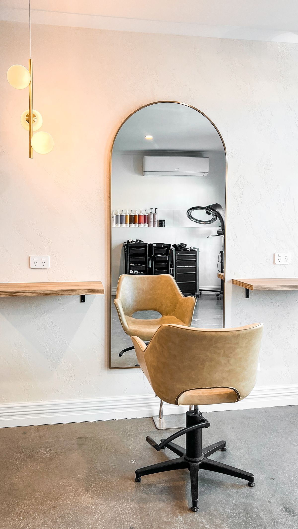 A styling station at Sugarcoat Studios with a tan leather chair, arched brass mirror and warm blush walls