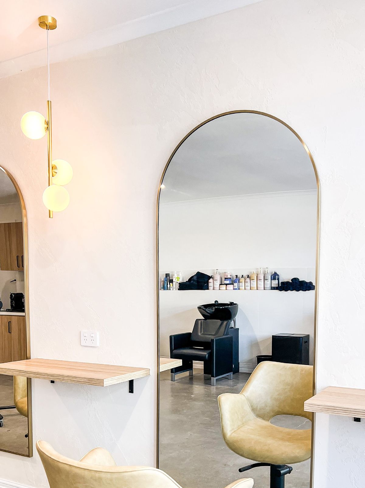 A row of arched brass mirrors and gold pendant lights with sunflowers in the foreground