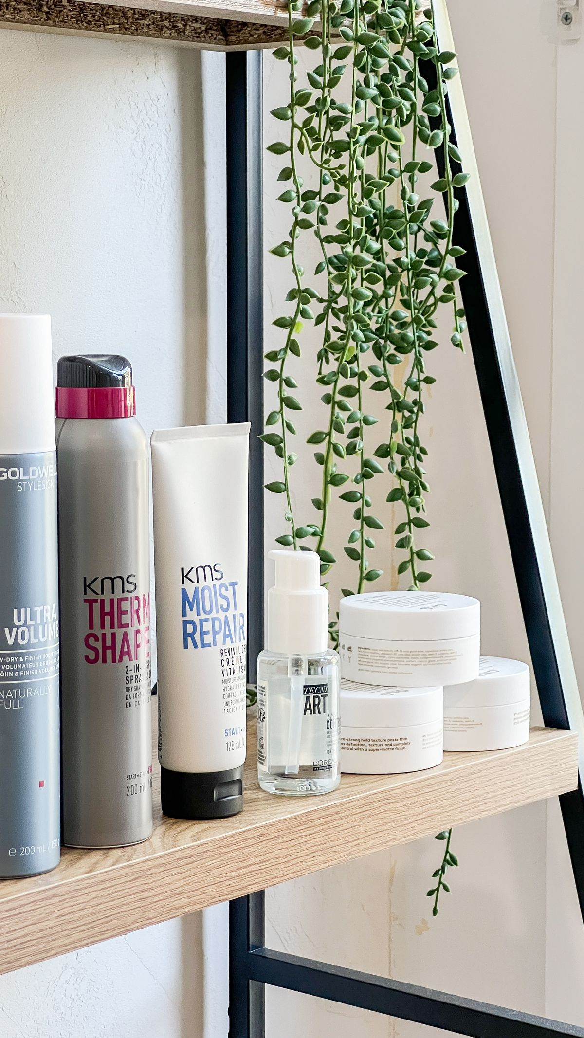 Styling products and a trailing plant on a light oak shelf