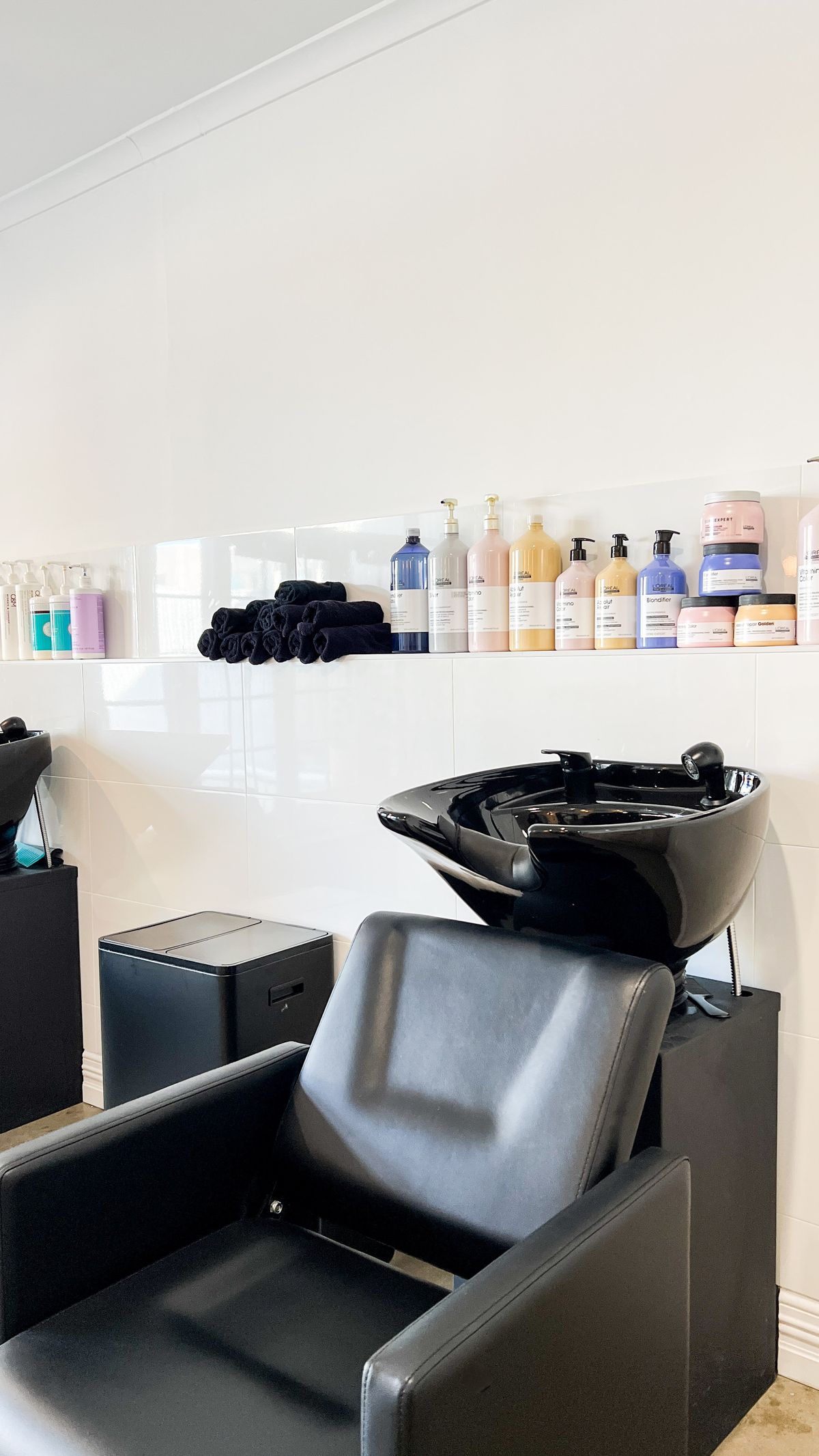 Professional black wash basin with a shelf of salon-grade hair products